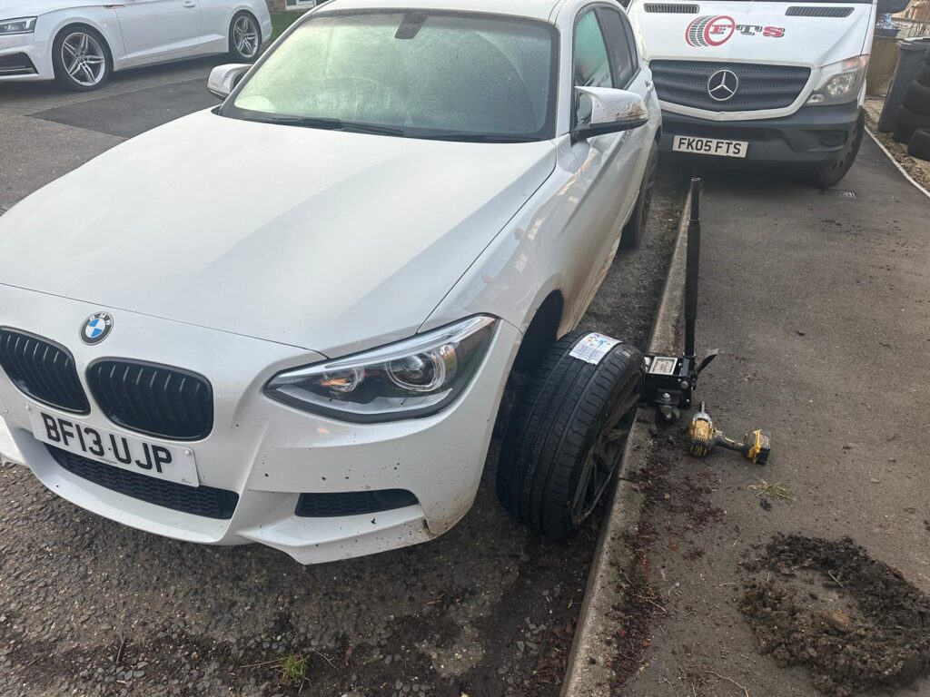 "Close-up of a mobile tyre fitting service van with a mechanic changing a car tyre on the roadside. The van is stocked with tools and replacement tyres, emphasizing convenience and on-the-go service."