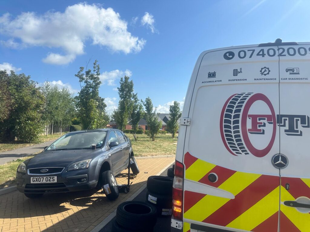 "Close-up of a mobile tyre fitting service van with a mechanic changing a car tyre on the roadside. The van is stocked with tools and replacement tyres, emphasizing convenience and on-the-go service."